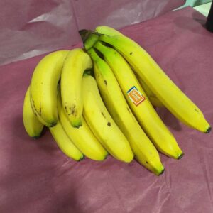 Grande grappe de bananes jaunes mûres sur un fond violet. Un autocollant "Bonanza Bananas" est visible sur l'une d'elles.