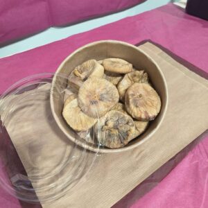 Bol en papier rempli de figues séchées dorées, avec un couvercle transparent ouvert, posé sur du papier kraft brun.