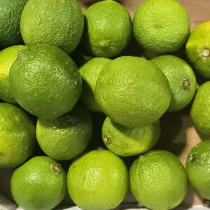 Tas de limes vertes fraîches et juteuses, à la peau rugueuse, empilées en gros plan sur un fond clair.