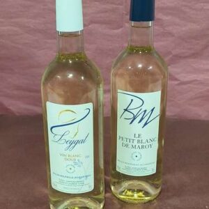 Deux bouteilles de vin blanc: Leygal Vin Blanc Doux (bouchon blanc) et BM Le Petit Blanc de Maroy (bouchon bleu foncé) sur fond uni.