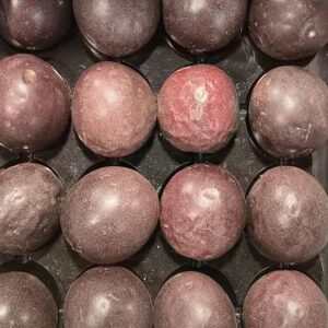 Plusieurs fruits de la passion mûrs, aux teintes violettes et rouges, disposés dans des compartiments noirs.