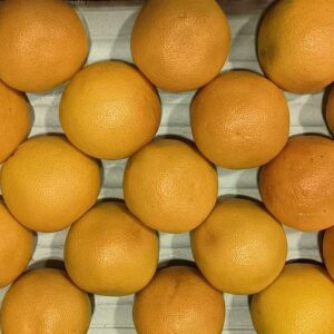 Nombreux pamplemousses frais à la peau orange/jaune, serrés dans un emballage quadrillé. Vue d'en haut.