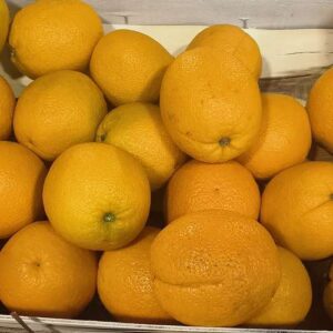 Gros plan sur un tas d'oranges juteuses et fraîches, empilées dans une caisse blanche. Les agrumes sont d'un jaune vif.