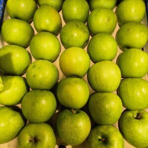 De nombreuses pommes vertes Granny Smith brillantes et fraîches, empilées dans un emballage en carton clair.