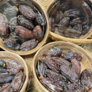 Plusieurs barquettes de dattes Medjool séchées, brun foncé et ridées, sous film plastique transparent, posées sur des paniers tressés.
