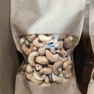 Sac kraft transparent rempli de noix de cajou. Les noix sont entières et certaines légèrement cassées.