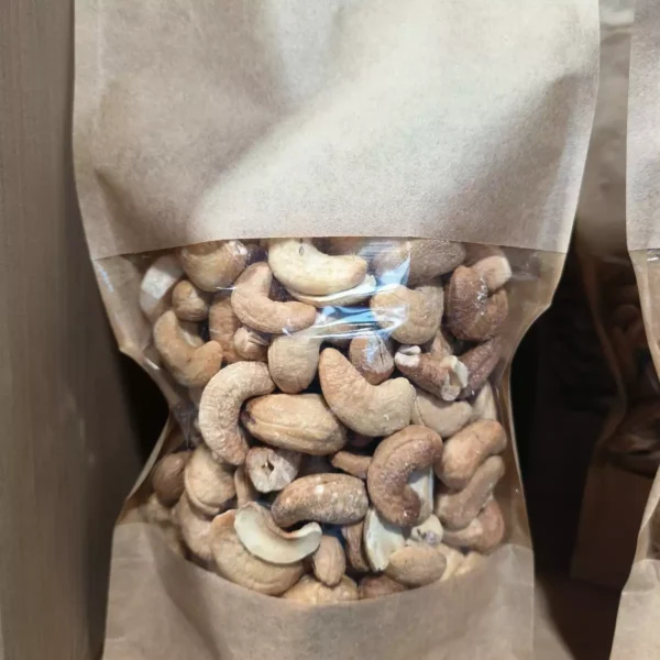 Sac kraft transparent rempli de noix de cajou. Les noix sont entières et certaines légèrement cassées.