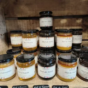 Assortiment de pots de miel APISPHERE de Périgord: Châtaignier, Acacia, Forêt, Tournesol, Fleurs, présentés sur des étagères en bois.