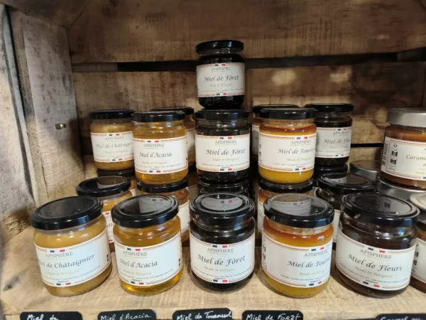 Assortiment de pots de miel APISPHERE de Périgord: Châtaignier, Acacia, Forêt, Tournesol, Fleurs, présentés sur des étagères en bois.