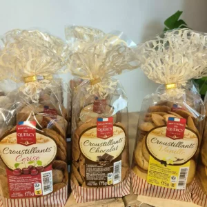 Trois sacs de biscuits Croustillants Biscuiterie du Quercy, saveurs Cerise, Chocolat et Vanille, chacun de 175g. Emballages transparents avec rubans dorés.