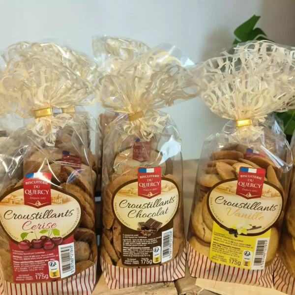 Trois sacs de biscuits Croustillants Biscuiterie du Quercy, saveurs Cerise, Chocolat et Vanille, chacun de 175g. Emballages transparents avec rubans dorés.
