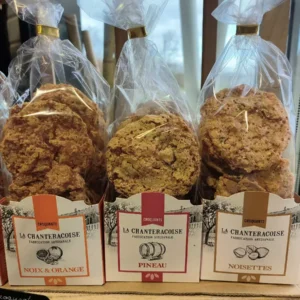 Sacs de croquants La Chanteracoise Fabrication Artisanale : Noix & Orange, Pineau, Noisettes. Biscuits dorés en sachets transparents sur étal.
