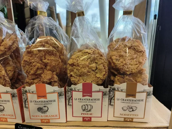Sacs de croquants La Chanteracoise Fabrication Artisanale : Noix & Orange, Pineau, Noisettes. Biscuits dorés en sachets transparents sur étal.