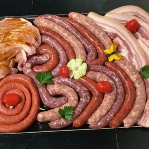 Grand plat de boucherie avec un assortiment de saucisses crues, poitrine de porc tranchée et viandes marinées, prêt pour grillades.
