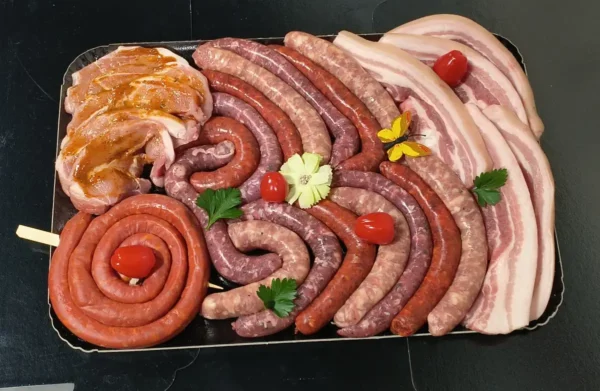Grand plat de boucherie avec un assortiment de saucisses crues, poitrine de porc tranchée et viandes marinées, prêt pour grillades.
