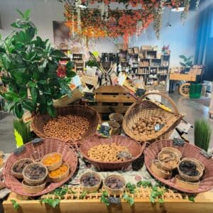 Présentoir de fruits secs et noix en vrac dans un magasin, avec des paniers de noisettes, amandes, noix, prunes, abricots, figues et dattes. Prix visibles.