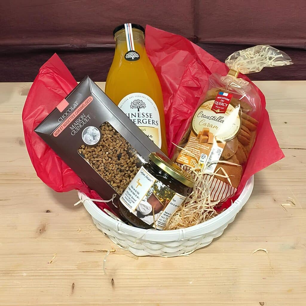 Panier cadeau garni de jus, chocolat noir noisettes Maison Guinguet, biscuits "Croustilla Caram" Quercy et pot. Posé sur bois.