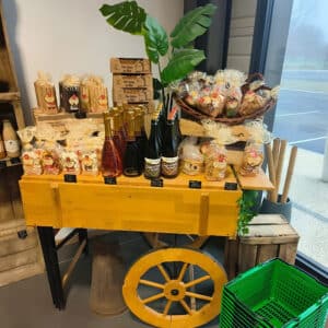 Présentoir de produits locaux: pain d'épices au miel, boissons Coup de cœur, biscuits et friandises sur un chariot en bois. 3.50€.