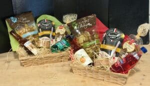 Deux coffrets gourmands en osier remplis de produits régionaux : chips de l'Aveyron, mini sticks, terrine de canard, biscuits chocolat et boissons artisanales.