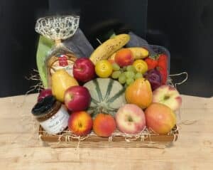 Corbeille gourmande garnie de fruits frais (melon, pommes, poires, bananes, fraises, raisins, pêches), miel et biscuits Quercy.