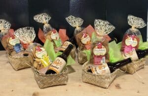 Sept paniers cadeaux tressés avec biscuits Croustillants (Biscuiterie du Quercy) saveurs variées et bières Effrontad sur bois clair.
