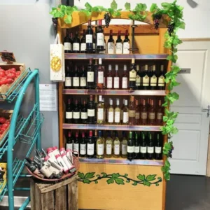 Présentoir en bois de vins rouges, rosés, blancs et petites bouteilles, décoré de vigne. Panier de tomates frais. Panneau 'Privé'.