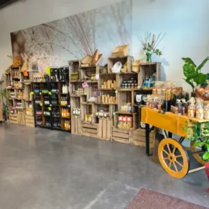 Étal de produits locaux sur caisses en bois et charrette: boissons, confitures, miel. Décor mural champêtre.