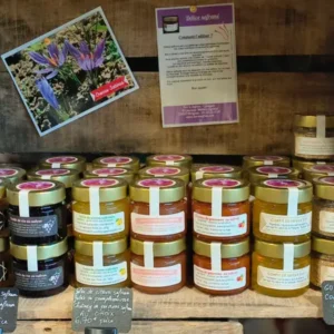 Étalage de produits au safran: confitures, gelées, chutneys, vinaigres. Carte 'Crocus Sativus', pancarte 'Délice safran' et prix 6,70€.